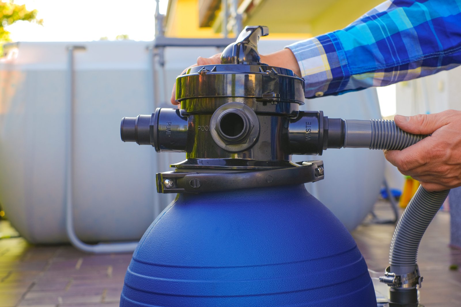 pool Filter. Swimming pool cleaning equipment.Blue water filter in the hands of a man in a blue plaid shirt on terrace .man moves the hoses to the filter in the pool close-up.